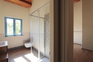 Casa di campagna - interno - bagno per gli ospiti con tetto in legno e luminosissima finestra di colore blu - vista di scorcio su camera da letto degli ospiti