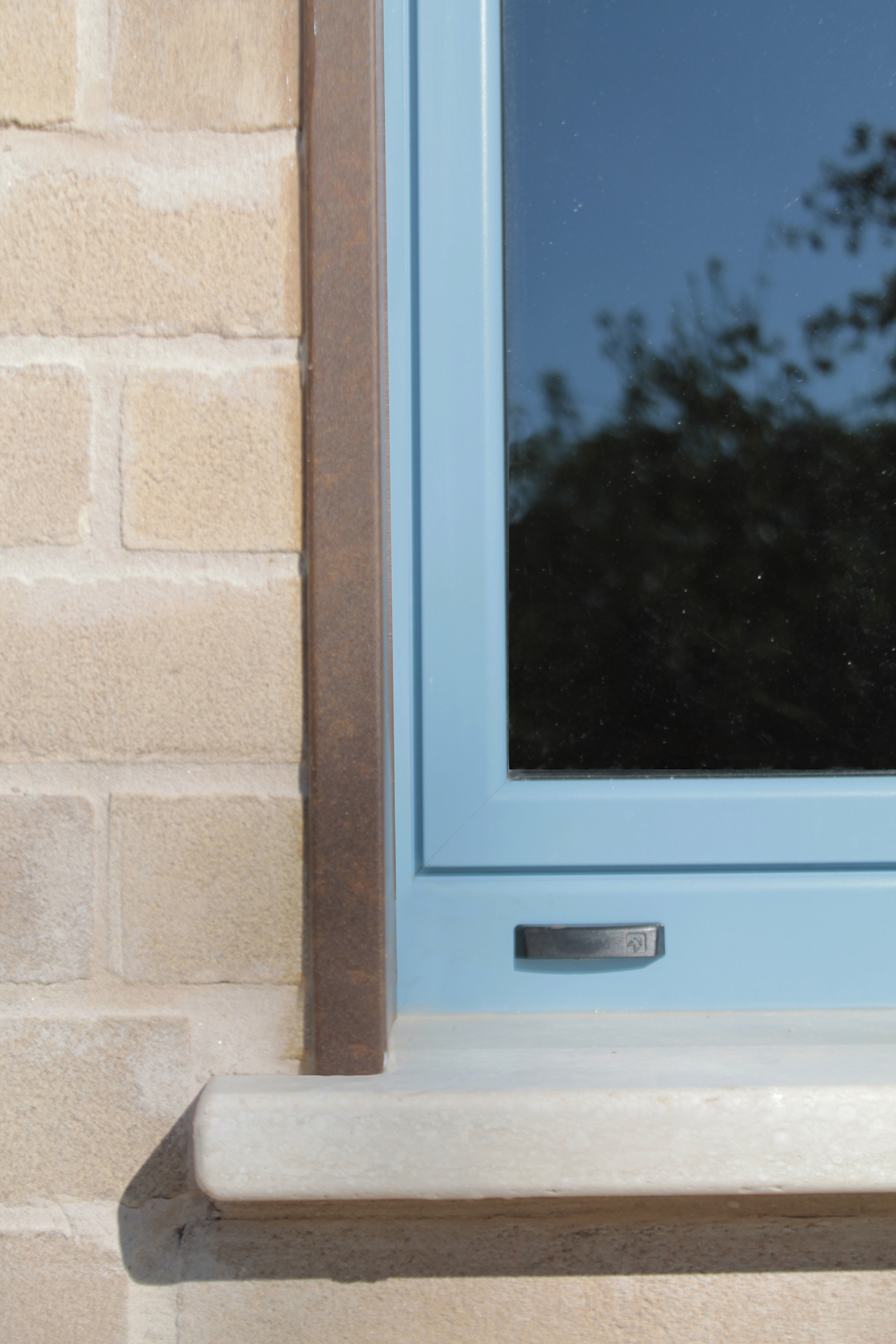 Casa di campagna - esterno - dettaglio della finestra del magazzino con infisso blu, soglia in travertino bocciardato e stipite in lamiera effetto acciaio corten parete in mattoni - pomeriggio di sole