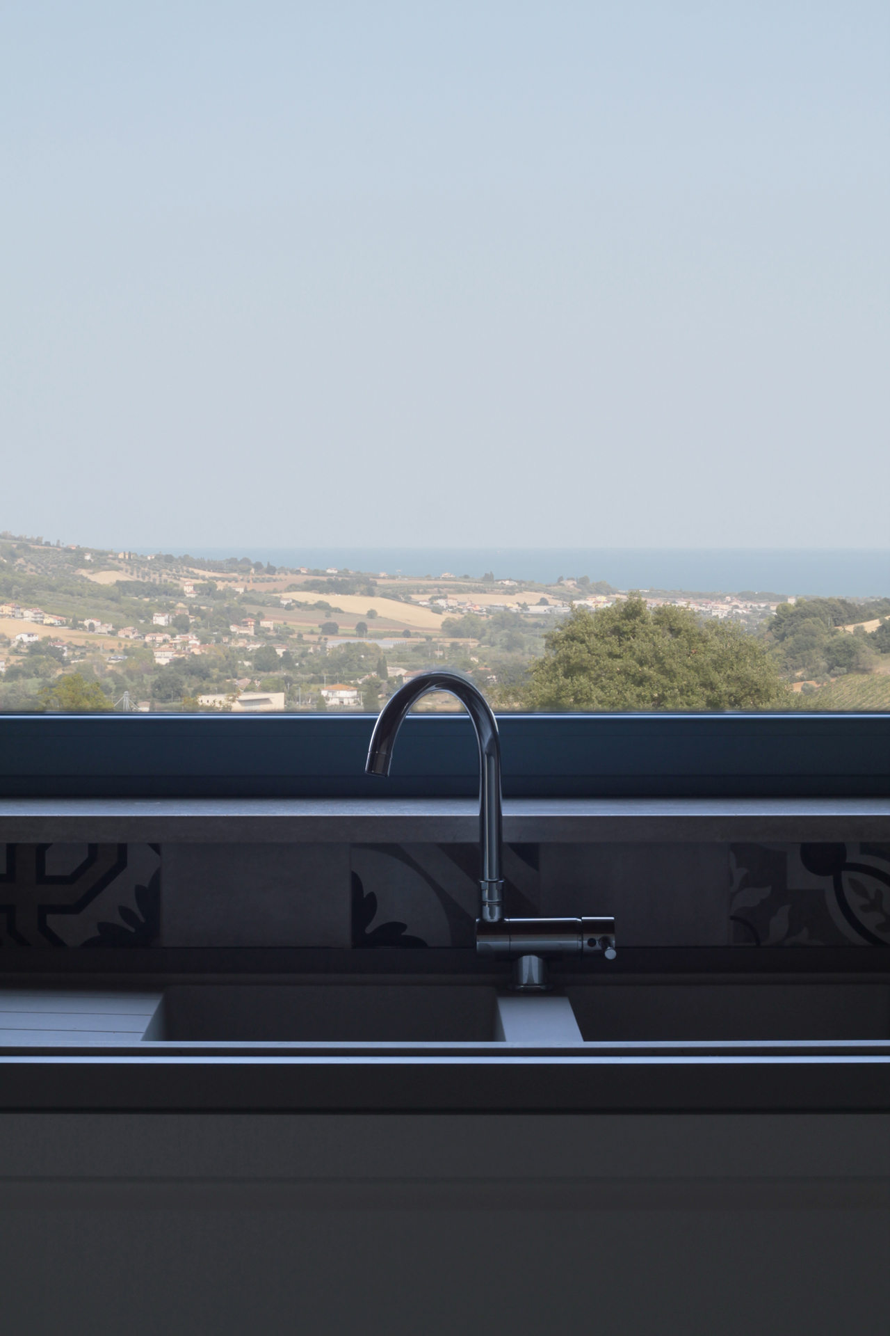 Casa di campagna - interno - dettaglio della finestra posta sopra il piano di lavoro della cucina fuori dalla quale si osserva il paesaggio che degrada verso il mare adriatico ben visibile sullo sfondo