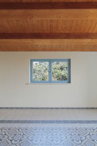 Casa di campagna - interno - scorcio del soggiorno con finestra blu aperta sulla natura e pavimento con disegno a tappeto realizzato con gres effetto cementina - soffitto in legno